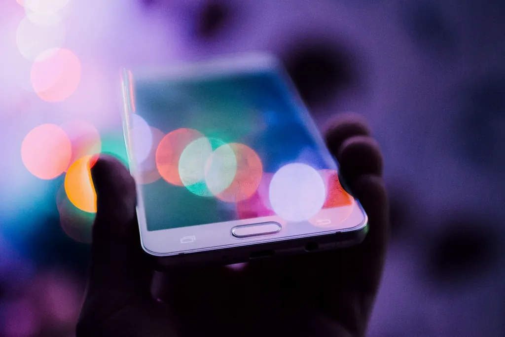 Manos con un smartphone bajo luces de colores, tragamonedas gratis en el móvil
